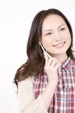 Beyaz arka planda izole edilmiş, gülümseyen ve cep telefonuyla konuşan güzel genç bir kadının portresi.