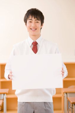 Asyalı erkek öğrenci sınıfta boş beyaz tahta tutuyor.