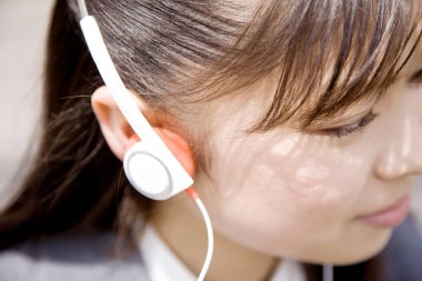 Genç Asyalı kadın kulaklıkla müzik dinliyor.