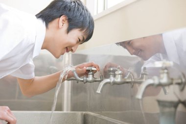 Sokak çeşmesinden su içen Asyalı genç adam.