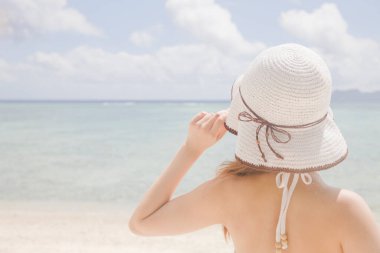 Sahilde poz veren beyaz şapkalı güzel bir kadın.