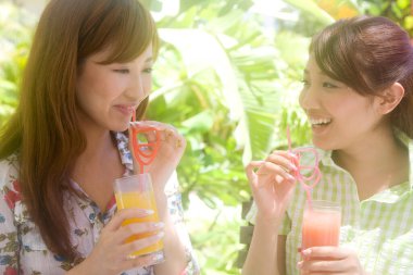 İki genç Asyalı kadın yaz bahçesinde kokteyl içiyor.