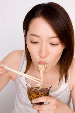 Asyalı kadın kaseden erişte yiyor ve çubuk kullanıyor. 