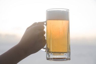 Kadın eli dışarıda bira bardağı tutuyor.