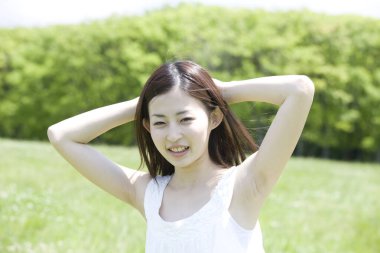 Güzel, genç bir Japon kadın. Ellerini başının arkasına koyup dışarıda kameraya gülümsüyor. 