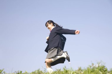 Okul üniformalı güzel bir Japon kızın portresi gökyüzü arka planında koşuyor.