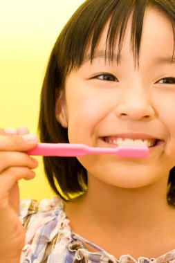 Asyalı kız sarı arka planda dişlerini fırçalıyor.