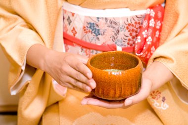 Geleneksel kimono giyen bir kadının ahşap çay içerken çekilmiş bir fotoğrafı. 