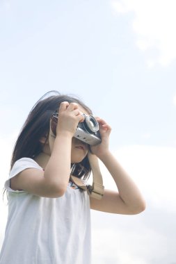 Küçük Asyalı kız dışarıda fotoğraf makinesi kullanıyor.