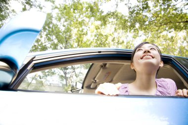 Güneşli bir günde araba camından bakan güzel, genç bir kadının portresi.