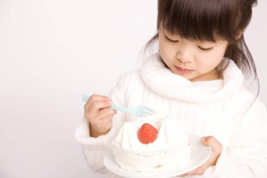 Beyaz stüdyo arka planında beyaz kremalı ve çilekli pasta yiyen küçük Japon kız.