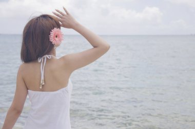 Pembe saçlı Asyalı kadının arkadan görünüşü deniz manzarasının keyfini çıkarıyor. 