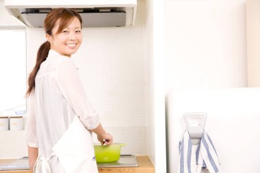 Genç Asyalı ev hanımı mutfakta yemek pişiriyor.