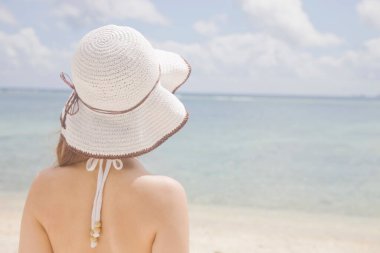 Sahilde poz veren beyaz şapkalı güzel bir kadın.
