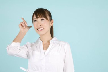 Güzel, genç Asyalı bir kadın, mavi arka planda parmak iziyle işaret ediyor.