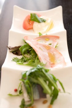 Beyaz tabakta lezzetli yemekler, dilimlenmiş jambon ve roka yaprakları.