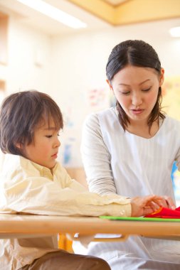 Genç bayan öğretmen ve tatlı Asyalı çocuk Japon anaokulunda kağıt origami yapıyorlar.