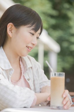 Asyalı genç kadın buzlu kahve içiyor ve kameraya bakıyor.