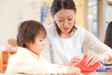 Genç bayan öğretmen ve tatlı Asyalı çocuk Japon anaokulunda kağıt origami yapıyorlar.