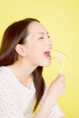 Sarı arka planda Baumkuchen yemek üzere olan Asyalı genç kadın.