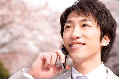 Baharda Sakura çiçeği açarken parkta telefonla konuşan genç Japon işadamının portresi.