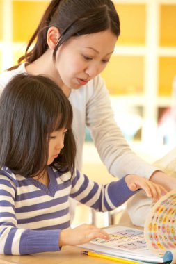 Küçük tatlı Asyalı kız Japon anaokulunda öğretmenle birlikte okuyor.