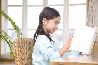 Küçük Asyalı kız kitap okuyor.