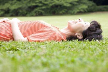 Olgun Asyalı kadın çimlerin üzerinde yatıyor.