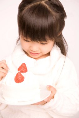 Beyaz stüdyo arka planında beyaz kremalı ve çilekli pasta yiyen küçük Japon kız.
