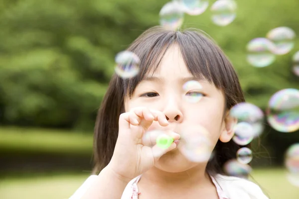 夏の公園で石鹸の泡を吹く小さなアジアの少女 — ストック写真