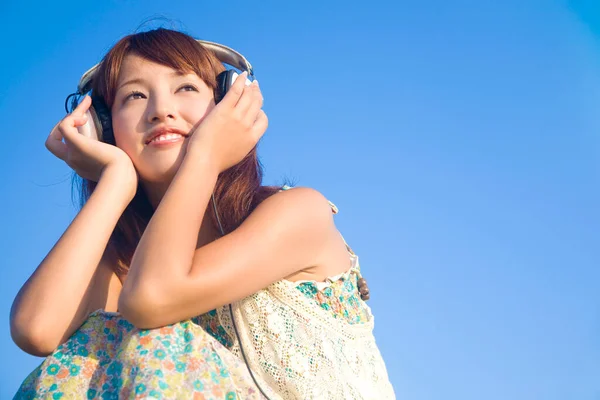 若い美しいアジアの女性は青い空の背景で音楽を聞きます — ストック写真