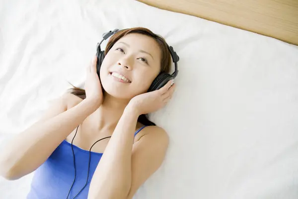 Genç Asyalı Kadın Yatağa Uzanıp Kulaklıkla Müzik Dinliyor — Stok fotoğraf