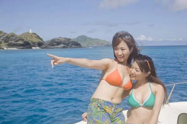 Pretty Japanese women in swimsuits resting on beach at daytime, summer vacation concept