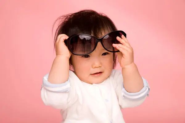 ピンクの背景にサングラスを持つアジアの少女 — ストック写真