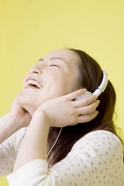 用黄色背景隔离的耳机听音乐的漂亮日本女人的肖像 — 图库照片