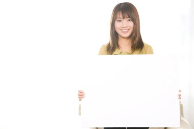 Güzel, genç Asyalı bir kadın elinde boş bir pankart tutuyor ve evde kameraya gülümsüyor. 