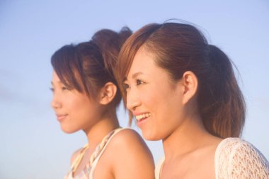 Mavi gökyüzüne gülümseyen iki güzel Asyalı kadın.