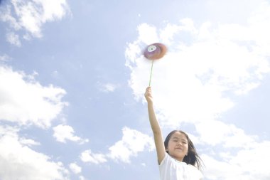 Küçük Asyalı kız mavi gökyüzüne karşı oyuncak tutuyor.