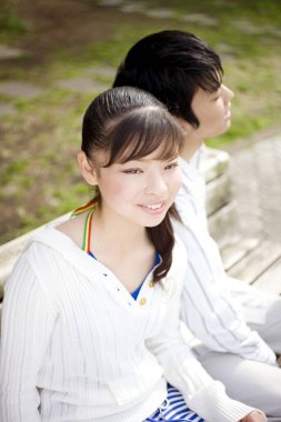 Genç Asyalı çift parkta oturuyor ve gülümsüyor.