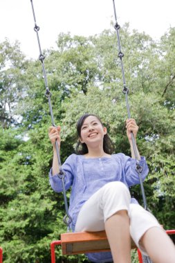 Genç Asyalı kadın parkta salıncakta oturuyor.