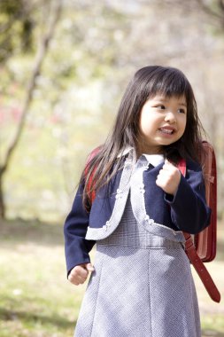 Kırmızı sırt çantalı Asyalı küçük kız bahar parkında yürüyor. 