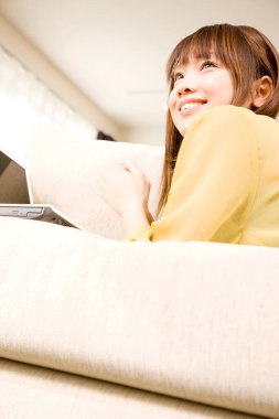 Güzel Asyalı kadın gülümsüyor ve evde laptop kullanıyor.    