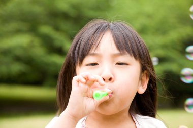 Küçük Asyalı kız yaz parkında sabun köpüğü üflüyor.