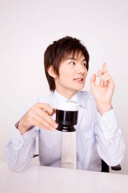 Genç Asyalı iş adamı, fincanı izole edilmiş arka planı işaret ediyor. 