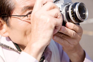 Üst düzey Asyalı adam dışarıda kamerayla fotoğraf çekiyor.