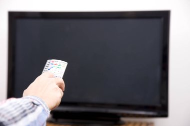 Uzaktan kumandayla televizyon izleyen bir kadın eli 