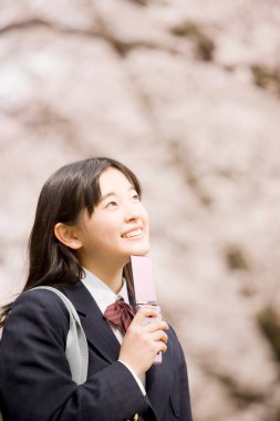 Çiçek açan kiraz ağacının arka planında okul üniformalı güzel bir Japon kız.