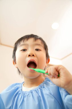 Küçük Asyalı çocuk banyoda dişlerini fırçalıyor.