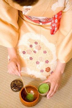 Geleneksel Japon çay töreninde kimono giyen ve matcha çayı hazırlayan bir kadın.   