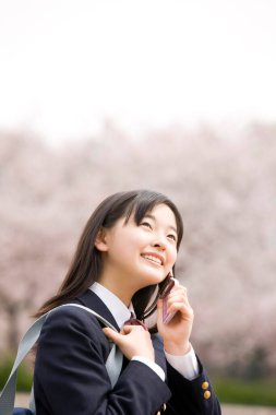Çiçek açan kiraz ağacının arka planında okul üniformalı güzel bir Japon kız.